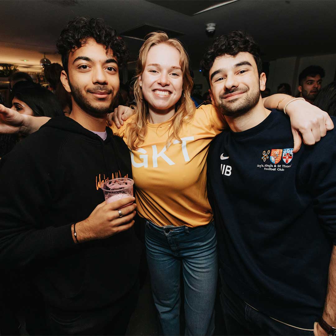 Three students smiling at the camera with their arms around each other