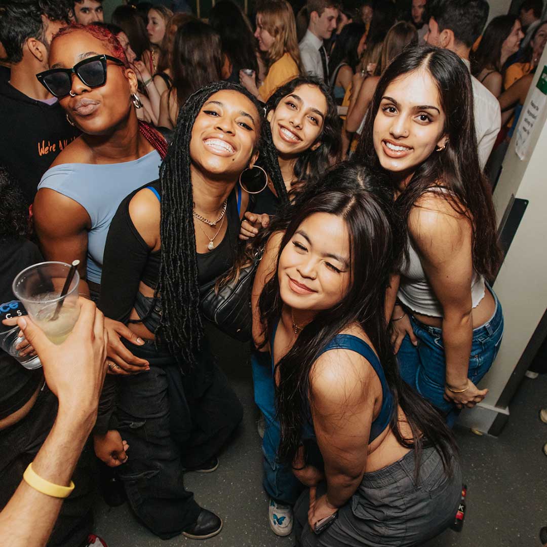 Five students smiling at the camera, one is wearing shades and another is winking