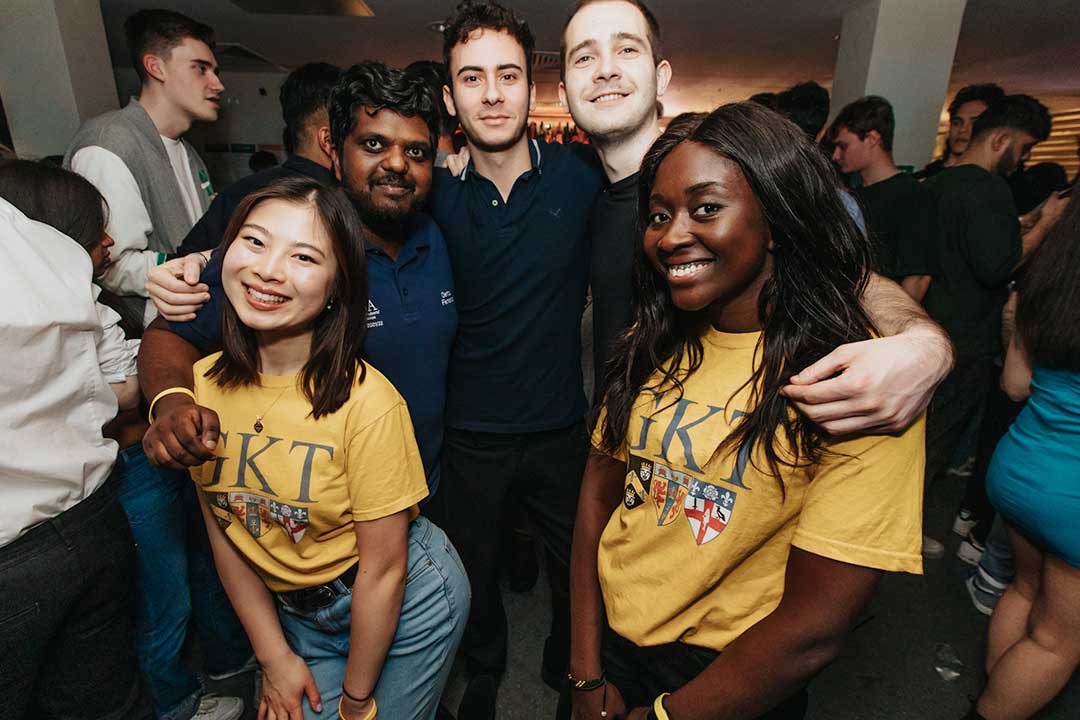 Five students smiling at the camera, the two at the front are wearing yellow GKT t-shirts